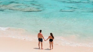 Un couple se tenant la main sur une plage, avec une eau turquoise et cristalline.
