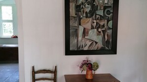 A room with a wooden chair, a small wooden table with a vase of flowers, and a framed abstract painting on the wall. - Apartment in medieval castle from the 14th century on the Weser cycle path (Petershagen)