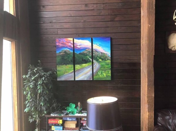 Une pièce avec un mur en bois, un tableau représentant une route, une lampe et une plante.