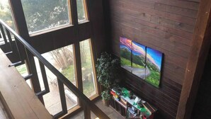 Une pièce spacieuse avec de grandes fenêtres, un plancher en bois, un téléviseur fixé au mur et une petite plante sur le rebord de la fenêtre.