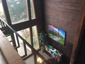 A spacious room with large windows, a wooden floor, a TV mounted on the wall, and a small plant on the windowsill.