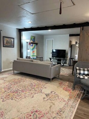 Un salon avec un canapé, un téléviseur et un tapis à motifs.