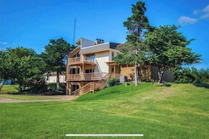 A two-story house with a balcony, a covered porch, and a large yard. - The Ranch: Lodge+Barn+Pool+Airstream • 35 Pax (Medicine Park)