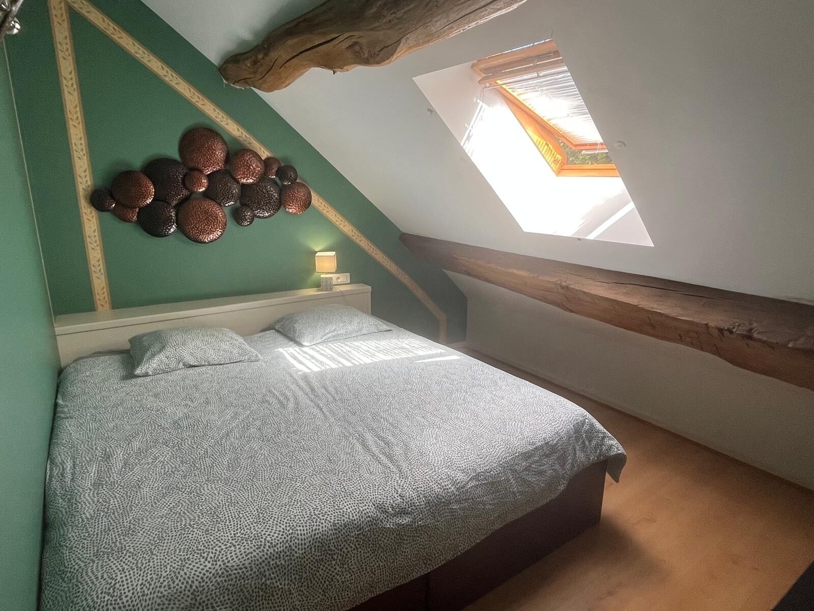 A bedroom with a sloped ceiling, a skylight, a bed with patterned bedding, and a wall-mounted decorative item.