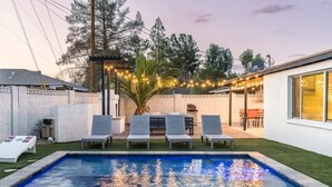 Un pati amb piscina, gandules, zona de barbacoa i llums penjants.