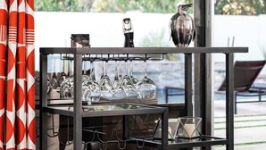 A bar cart with wine glasses and a pitcher, positioned near a window with a view of greenery. - Turquoise Retreat - Pool, Putting Green, Location! (Scottsdale)