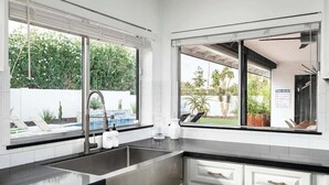 A modern kitchen with a large window, a built-in sink, and a view of a pool and greenery. - Turquoise Retreat - Pool, Putting Green, Location! (Scottsdale)