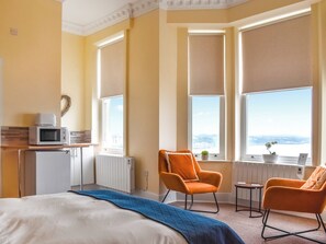 A hotel room with a bed, two orange armchairs, a small table, a microwave, and a radiator. - Denelea Studio 2 - UK49953 (Scarborough)