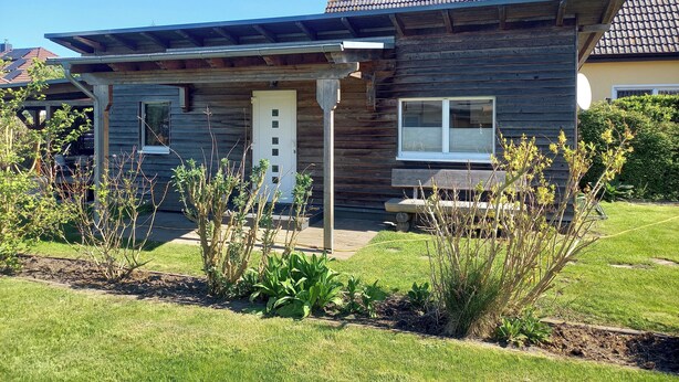 Une maison moderne avec une façade en bois, une porte blanche et un porche abrité.