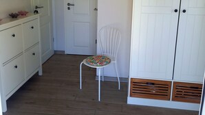 Une pièce avec une armoire blanche, une chaise blanche, une porte blanche et une commode blanche dotée de tiroirs.