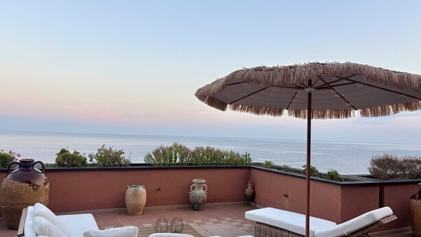 A balcony with a view of the sea, featuring a lounge area with cushions and a wicker chair, and two large vases. - Welcome to your Seaside Home (Varazze)