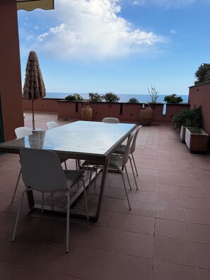 Eine Terrasse im Freien mit Tisch und Stühlen, einer großen Vase und Blick auf das Meer.