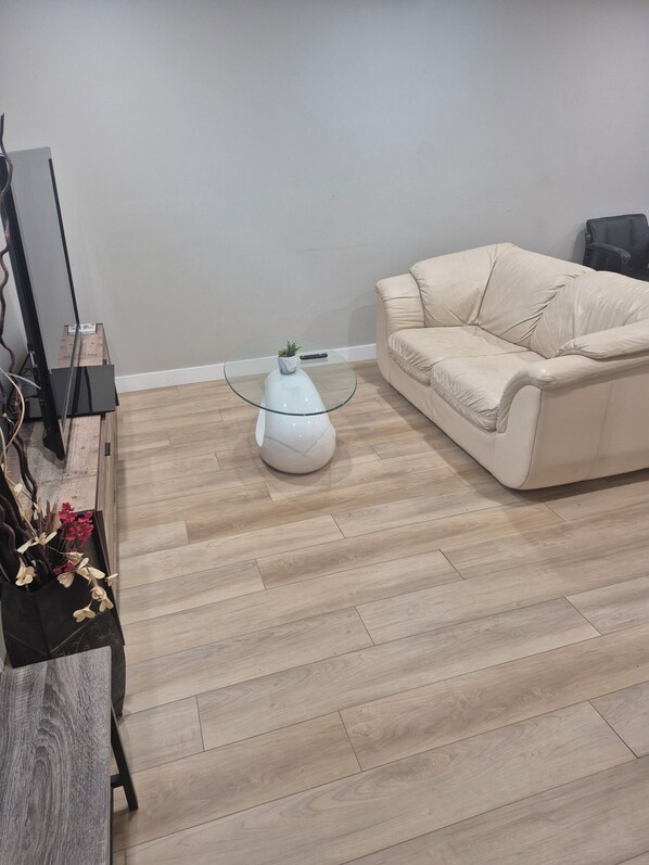 A living room with a glass coffee table, a beige sofa, and a wooden floor.
