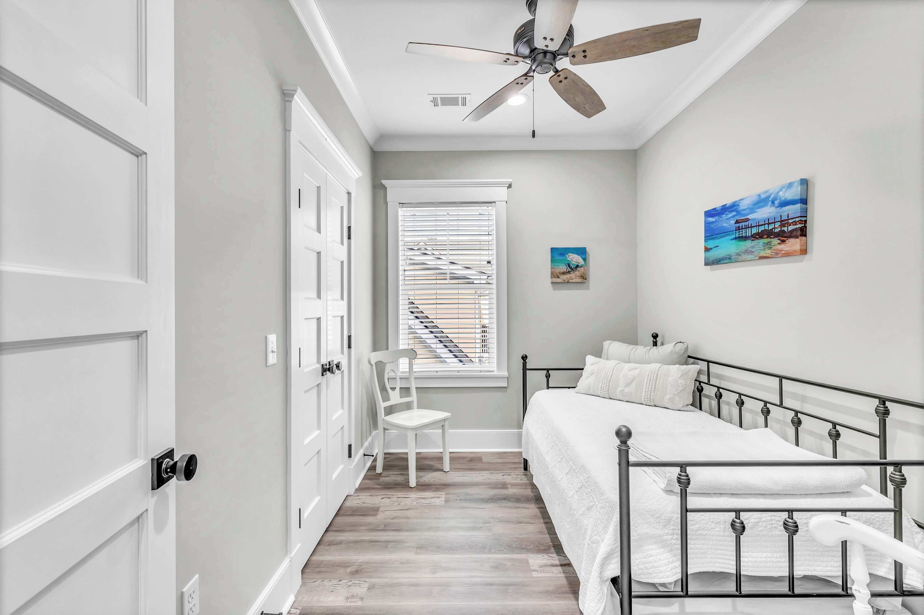 A bedroom with a bed, a chair, a window with blinds, a ceiling fan, and a painting on the wall.