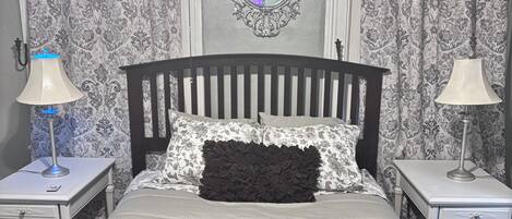 A bedroom with a wooden bed, two nightstands, a mirror, and patterned curtains.