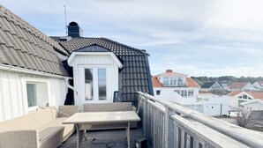 A deck with wicker furniture and a table, overlooking a residential area with houses. - 4 Star Holiday Home in Hono (Hono)