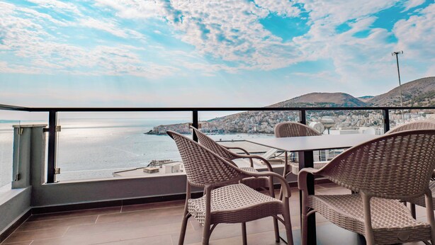 Un balcone con sedie in vimini e un tavolo che si affaccia su una città costiera.