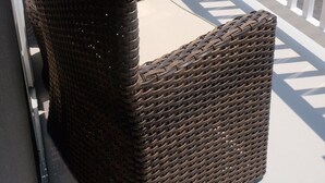 Una silla de mimbre con cojín en un balcón con baranda blanca.