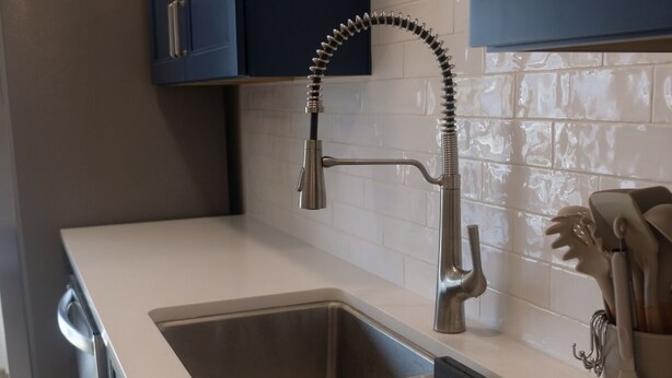 Una cocina con un lavamanos de acero inoxidable, armarios oscuros y salpicadero de azulejos blancos.