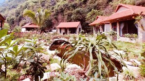 A rustic mountain lodge with multiple red-roofed cabins, a small bridge over a stream, and lush greenery.