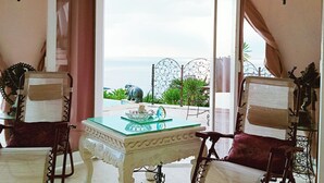 A room with a glass-top table, two upholstered chairs, a decorative mirror, and a view of the ocean. - VistaMonti Private Villas (Pemenang)