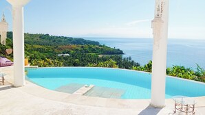 A pool area with two columns, a glass table, and a view of the sea and greenery. - VistaMonti Private Villas (Pemenang)