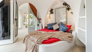 A bedroom with a red bedspread, multiple pillows, a patterned throw blanket, and a large mirror with floral decorations. - VistaMonti Private Villas (Pemenang)