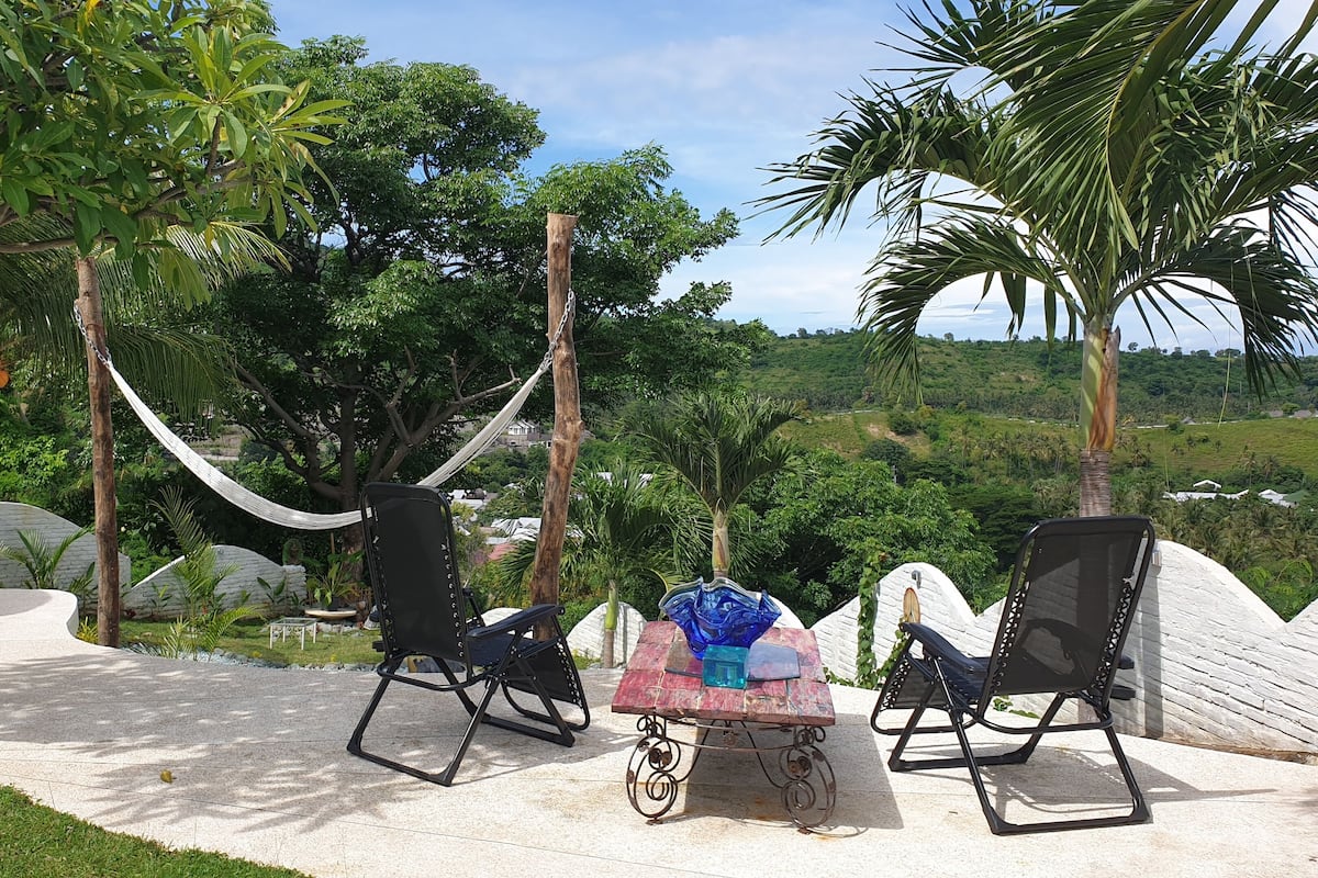 A patio with two black lounge chairs, a small table with a blue and red tablecloth, and a hammock.