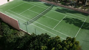 Ein Tennisplatz im Freien, umgeben von viel Grün und einer Steinmauer.