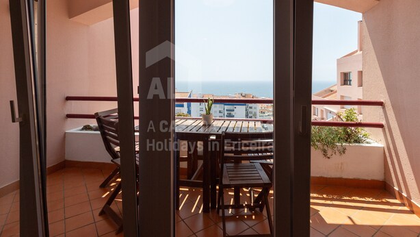 Ein Balkon mit Tisch und Stühlen, einem Blumentopf und Blick auf das Meer.