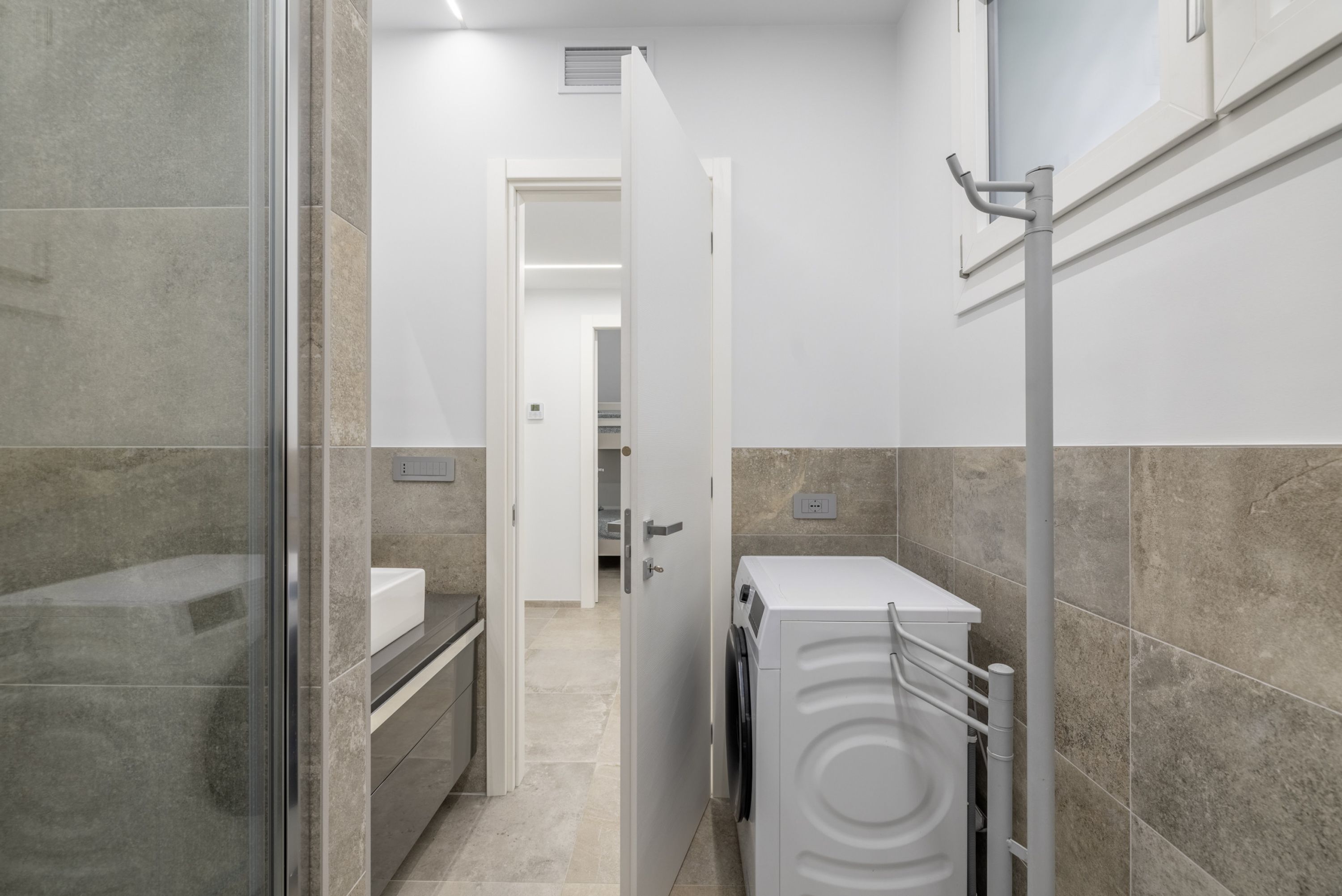 A modern bathroom with a glass shower enclosure, a built-in washing machine, and a white sink.