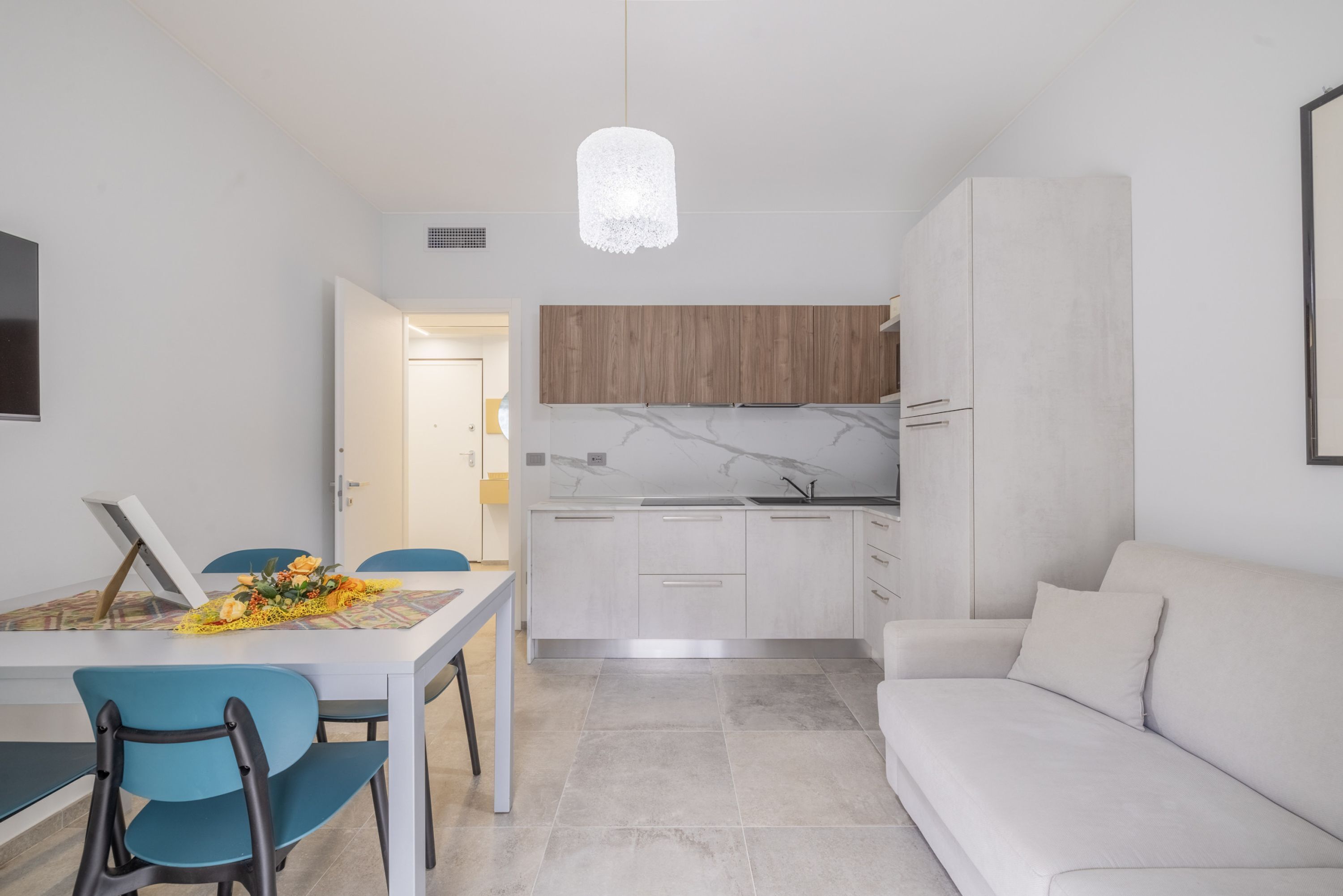 Una cocina moderna con gabinetes blancos, encimera de mármol y una lámpara colgante.