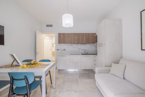 A modern kitchen with white cabinets, a marble countertop, and a hanging light fixture.