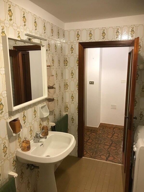 A bathroom with a white sink, mirror, and decorative tiles. There is a wooden door leading to another room.