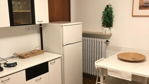 A compact kitchen with white cabinets, a white refrigerator, a small table with a bowl, and a radiator.