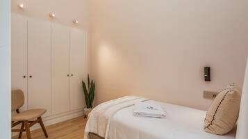 A bedroom with a bed, a chair, a wardrobe, a plant, and a wall-mounted light fixture.