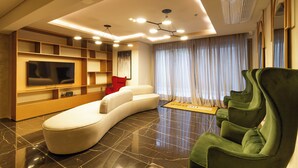 Una sala de estar moderna con un sofá curvo, un sillón verde, un televisor de pantalla plana y estanterías empotradas.