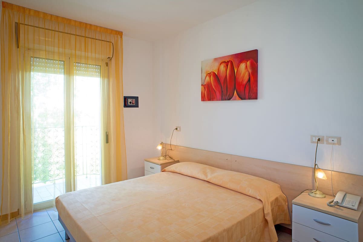 Une chambre à coucher avec un lit, des tables de chevet avec des lampes, un tableau au mur et une fenêtre avec des rideaux.
