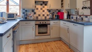 A compact kitchen with white cabinets, a microwave, a red refrigerator, and wooden flooring. - Clover Cottage (Saint Wenn)