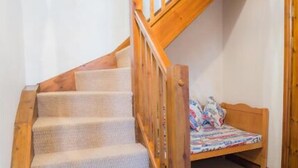 A wooden staircase with carpeted steps leading to a bedroom with a bed and a window. - Clover Cottage (Saint Wenn)