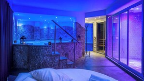 A modern spa room with a stone wall, a hot tub, and a bed with towels. - TPH Rooms (Taormina)