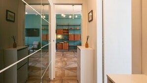 A hallway with a mirrored wall, wooden flooring, and a view into a room with teal walls and wooden shelves. - Bright one bedroom Porta Venezia - Mirable PM (Milano)