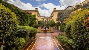 A courtyard with a paved pathway leading to a gated entrance, surrounded by lush greenery and buildings with a classic architectural style. - Bright one bedroom Porta Venezia - Mirable PM (Milano)