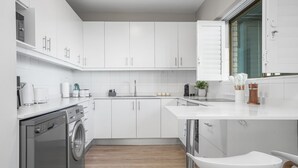A modern kitchen with white cabinetry, a built-in dishwasher, and a window with a view. - Searenity Tides - Two Bedroom Apartment, Sleeps 4 (Cape Town)