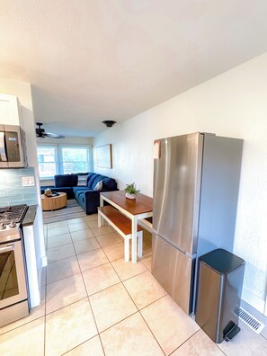 Una cocina moderna con un refrigerador de acero inoxidable, un microondas y una estufa. Hay un banco de madera y una pequeña mesa con una planta.