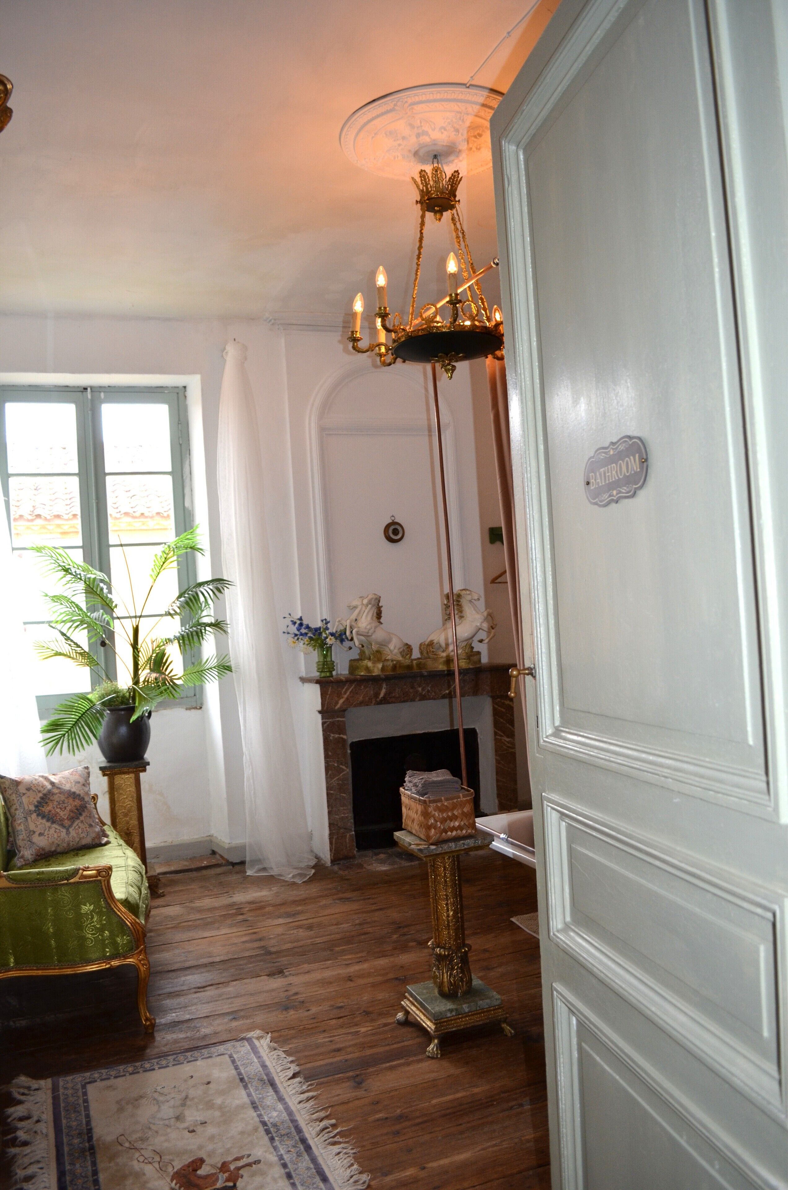 Une pièce avec une cheminée, un lustre, un canapé vert et une plante en pot.