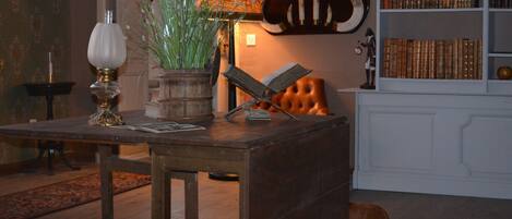 A cozy reading nook with a wooden table, a lamp, a potted plant, and a leather chair.