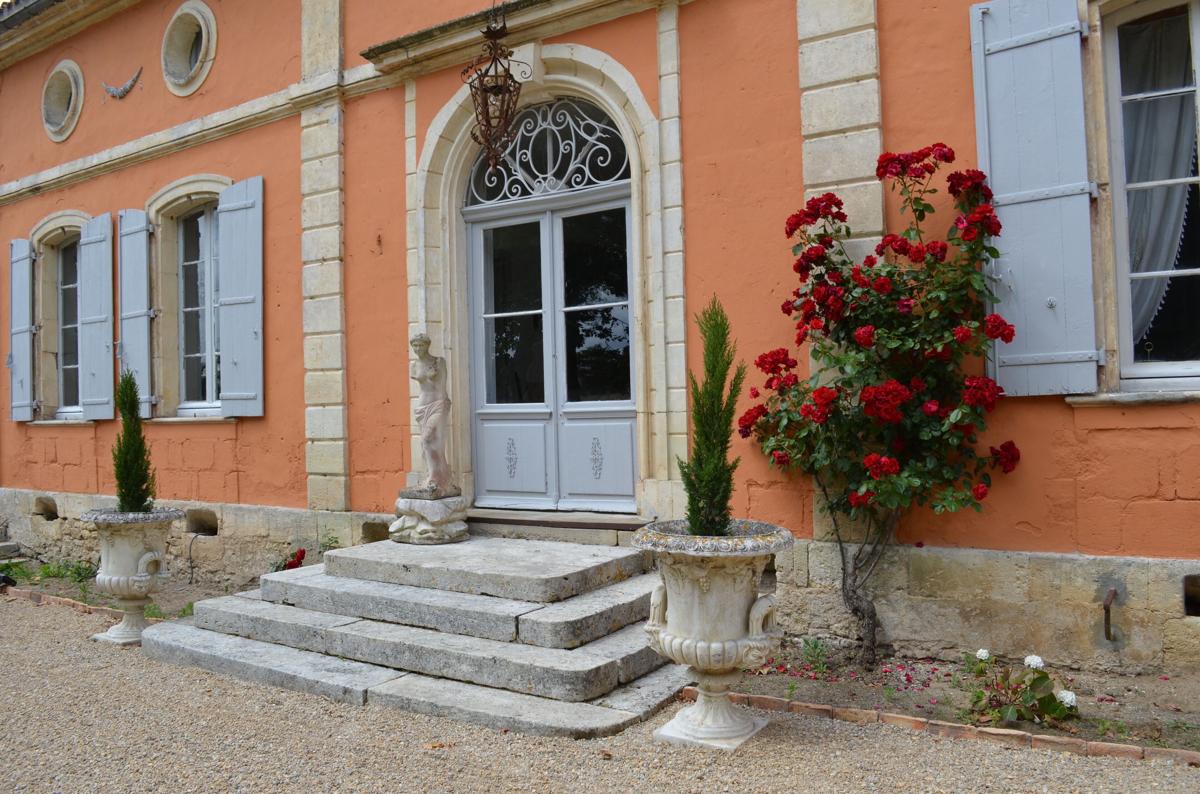 A building with a stone staircase leading to a door, a statue, and a flower bed with red flowers.