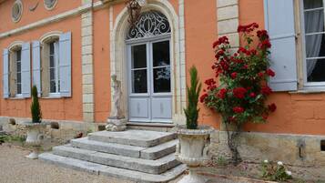 A building with a stone staircase leading to a door, a statue, and a flower bed with red flowers.