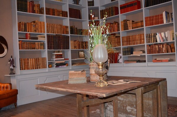 Una habitación con una mesa de madera, estanterías llenas de libros y un jarrón con flores.